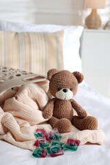 Laundry detergent capsules, teddy bear and basket with clean linens on bed indoors