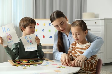 Speech therapist teaching little kids alphabet with magnetic letters and pictures at white table indoors