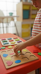 Fototapeta premium Toddler boy playing with a colorful wooden puzzle on a table in a bright kindergarten classroom