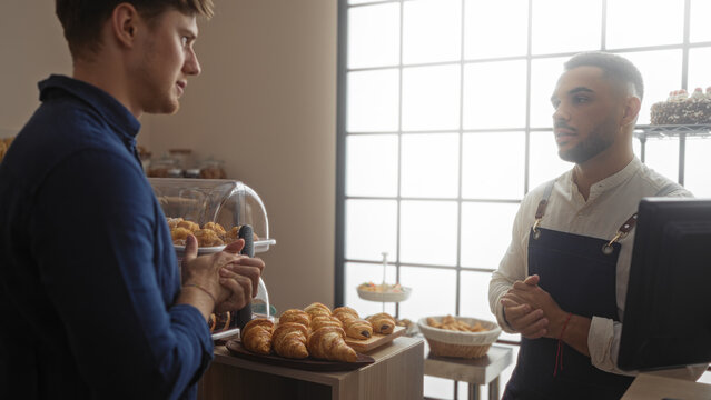 Men conversing inside a bakery room with various pastries displayed, featuring handsome male employees engaged in a professional dialogue indoors