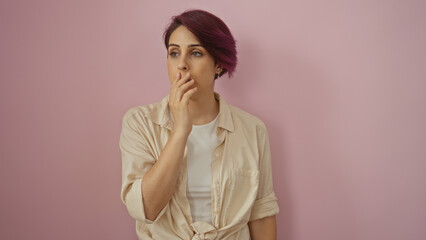 A young, beautiful caucasian woman with short hair covers her mouth with her hand, standing isolated against a pink background.