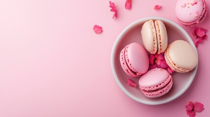 Pink and white macarons in bowl, with petals scattered around