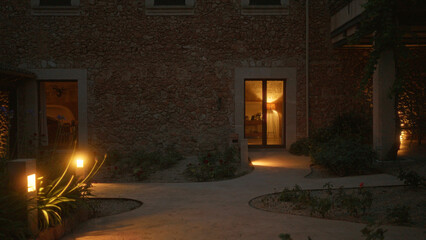Exterior view of a cozy, illuminated stone house at night, showing glowing garden path lights, warm...