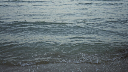Waves gently lap against the shore on an empty beach with a vast expanse of blue water under a serene sky, capturing the tranquility of the seaside