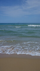 An idyllic seascape showcasing gentle waves lapping onto a sandy beach with a clear blue sky overhead.