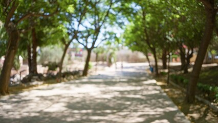 Blurred scene of an outdoor park with trees and shadows in the background creating a bokeh effect and a defocused path leading to a bright, sunny day