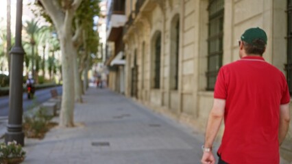 Man walking along a tree-lined urban street with blurred background and historic buildings in an...