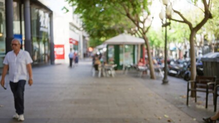 Defocused urban street with blurred man walking, outdoor cafe, and trees in bokeh background on a sunny day.