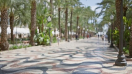 Defocused walkway in alicante, spain, showing palm trees and people enjoying a sunny day outdoors along the decorated promenade