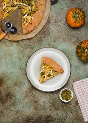 Sliced ​​savory gluten free galette with pumpkin, brie cheese and pumpkin seeds on buckwheat crust on ceramic plate on green concrete background.