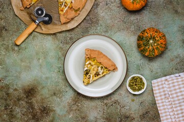 Sliced ​​savory gluten free galette with pumpkin, brie cheese and pumpkin seeds on buckwheat crust on ceramic plate on green concrete background.