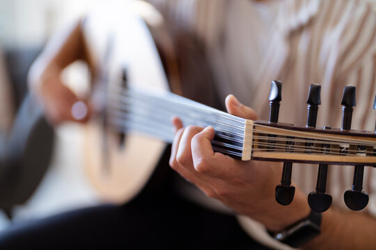 man’s hand skillfully strumming the strings of an oud, capturing the intricate design of the instrument and highlighting the delicate craftsmanship and cultural significance of the musical tradition.