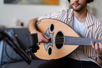 Close-up of a man wearing headphones, strumming an oud while recording in a cozy living room, capturing the essence of home music production and passion for musical creation.