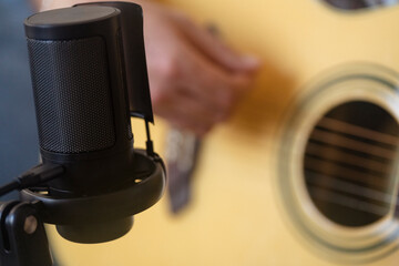 A focused image of a microphone set up next to an acoustic guitar, capturing the details of the equipment in a home recording environment, ideal for producing high-quality sound indoors.