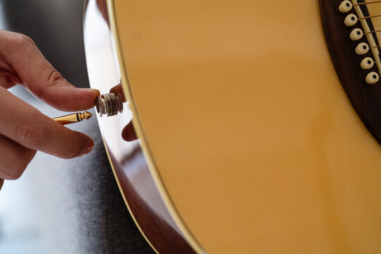 A close-up image showing a person&rsquo;s hand connecting a cable to a guitar, capturing the detail and care in setting up music equipment, emphasizing focus and precision in an indoor environment