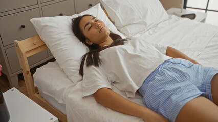 Obraz premium Young woman resting peacefully on a bed in a cozy bedroom, surrounded by simple, modern furniture and soft, natural light cascading through a nearby window