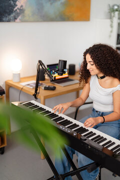 young woman is focused on her keyboard practice in a home studio, sitting by a microphone in a creative and professional setup that highlights her musical dedication and skill.