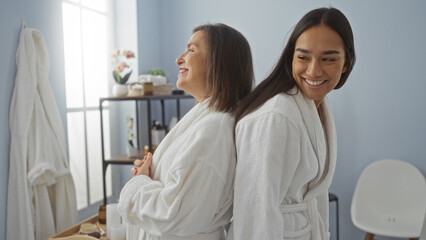 Women relaxing in a spa covered in white robes, mother and daughter sharing a joyful moment together indoors, portraying love and wellness in a calm salon setting.