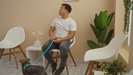 Young asian man sitting with his dog on a leash in a veterinary waiting room, looking to the side...