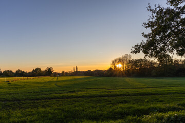 Sunset over a field with trees in the foreground and a church in the background