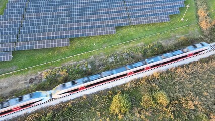 Modern electric train travelling beside solar panel farm. Aerial view