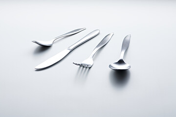 Silver colored cutlery such as spoons, forks, knives, cups and plates photographed against a white background