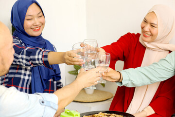 Happy Asian Muslim Family Drinking And Toasting Glass At Korean BBQ Style Party