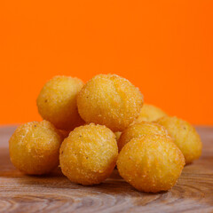 Pile of crispy breaded potato balls on a wooden surface against an orange background. Studio food photography. Snack and appetizer concept. Design for poster, banner, menu, wallpaper.