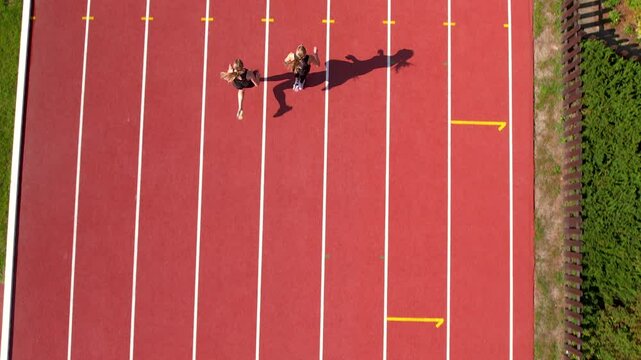 Two runners mid-stride on parallel track lanes, shadow stretching, capturing dynamic movement from above