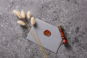 Envelope with wax seal and vintage stamp, dry lagurus flowers on dark gray concrete background....