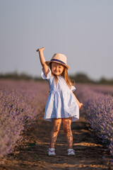 Little girl in in white and blue dress across field of purple lavender among the rows at sunset.