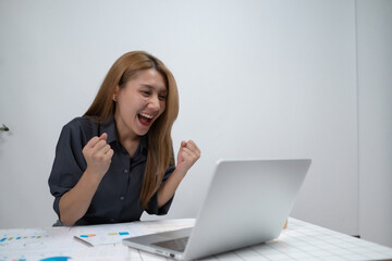 A woman is sitting at a desk with a laptop open and is smiling
