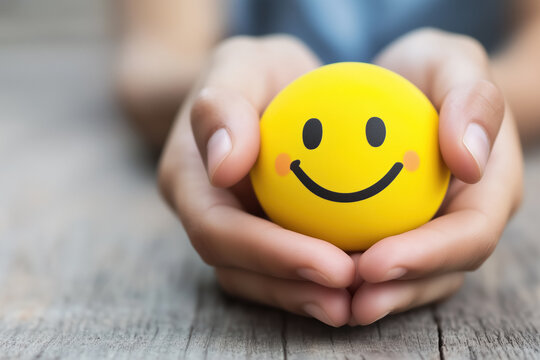 Close-up of hands gently holding a yellow smiley face ball, symbolizing happiness, positivity, and care. Ideal for mental health, encouragement, and support themes.