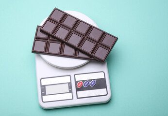 Dark chocolate bars with Kitchen scale on blue background. Calorie counting, diet, weight loss