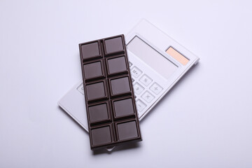 Dark chocolate bar with calculator on white background. Calorie counting, diet, weight loss