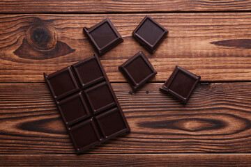 Blocks of broken chocolate bar on wooden background