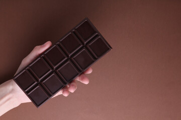 HAnd holding Dark chocolate bar on brown background
