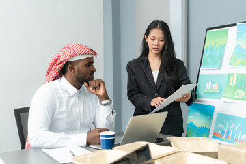 An Asian businesswoman and her Arab colleague engage in a focused discussion over financial charts in an office environment. She presented data in chart form to her Arab colleagues in office.