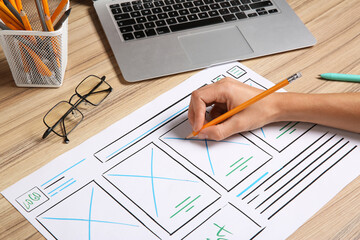 Developing UI design. Designer with smartphone creating website wireframe on paper at wooden table,...