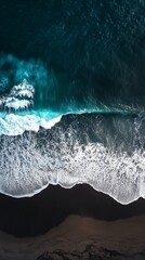 Fototapeta premium Aerial image showcasing ocean waves crashing onto a black sand beach, highlighting natural contrasts and serene coastal scenery.