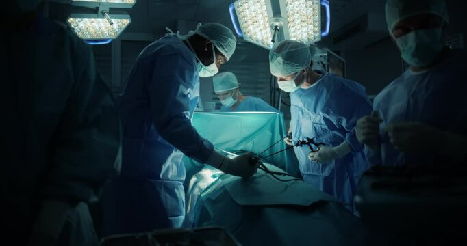 Dressed in Full Protective Gear, Diverse Surgeons and Nurses Coordinate as a Team Around the Operating Table, Saving Life of a Patient with Their Combined Skills and Medical Training