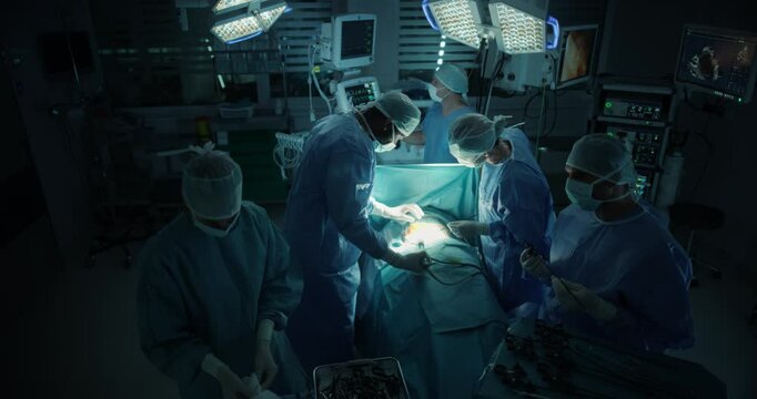 Diverse Surgical Team Working in a Darkened Operating Room Surrounded by Advanced Medical Equipment. Female and Male Doctors Performing a Complex Surgery in Order to Ensure Patient Safety