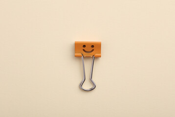 Binder clip with a smiling face on a beige background