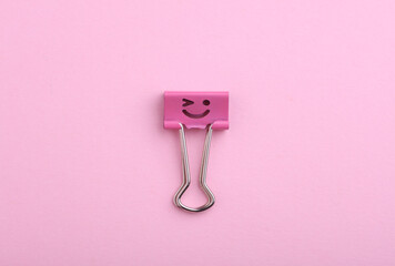 Binder clip with a smiling face on a pink background