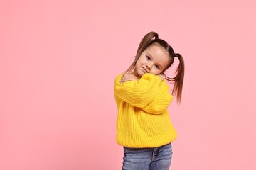 Cute little girl hugging herself on pink background, space for text