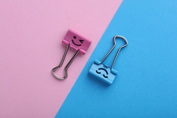 Binder clips with a smiling face on pink blue background. Business concept. Creative layout