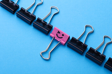 Binder clip with smiling face and faceless binders on blue background. Leadership, uniqueness,...
