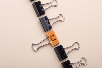 Binder clip with smiling face and faceless binders on beige background. Leadership, uniqueness, career growth. Business concept.