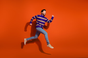 Full size photo of nice young male running fast wear trendy striped violet outfit isolated on orange color background
