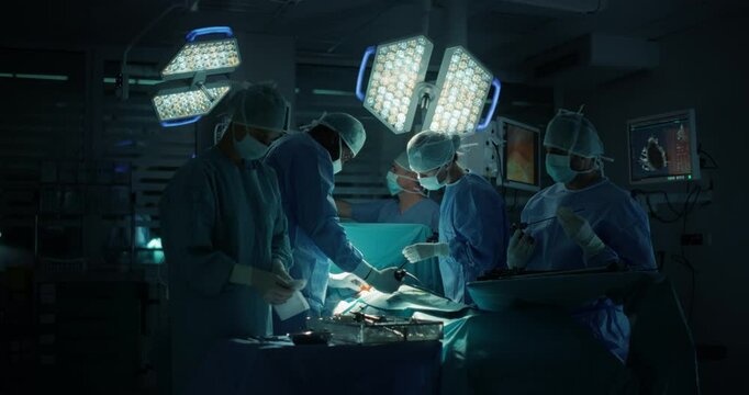 Medical Team Performing a Complex Surgery on a Patient, Using Specialized Tools, Looking at Digital Screens with Health Information. Doctors with a Female Surgeon in the Lead Saving Patient's Life
